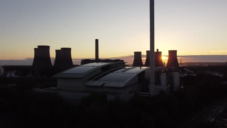 Sunrise-emerging-behind-silhouette-of-power-station-stacks-and-British-solar-energy-factory-aerial-push-in-view