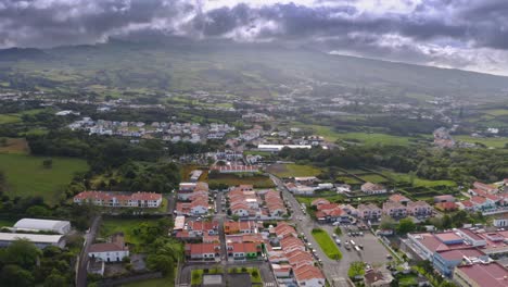 Dark-storm-clouds-over-town-in-Azores-mountain-foothills,-aerial-view