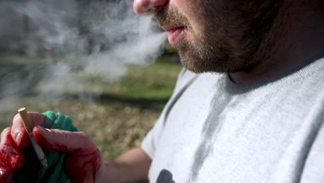 Close-up-Caucasian-man-With-bloody-hand-holding-and-smoking-a-cigarette,-Slow-motion