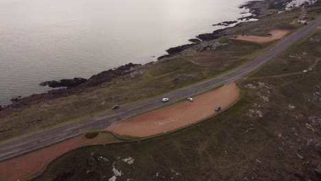 White-car-driving-along-coastal-and-panoramic-road-ocean-view,-Punta-Ballena-peninsula-in-Uruguay