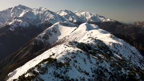 Mt-Fyffe-and-Southern-Alps-mountain-range-covered-in-snow,-aerial-reveal-of-Kaikoura-Peninsula-on-New-Zealand-shore