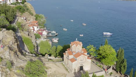 Drone-flying-up-and-over-St-John-Church-on-Lake-Ohrid-North-Macedonia-showing-lake-views-and-boats