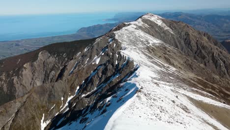 Drone-flying-over-mountain-ridge-covered-in-snow