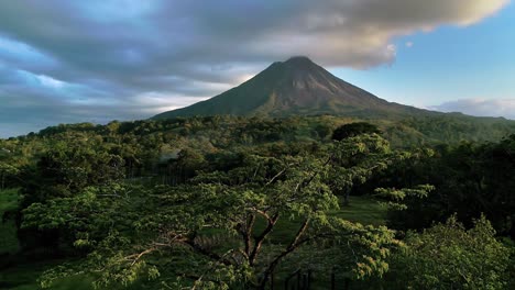 Drone-flying-over-tropical-and-lush-forest-at-sunset-with-Arenal-Volcano-in-background,-Costa-Rica