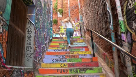 Mujer-Rubia-Europea-Subiendo-Enérgicamente-Las-Escaleras-Pintadas-De-Colores-De-Un-Callejón-Urbano