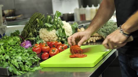 Unrecognizable-chef-slicing-red-tomato-on-cutting-board-in-restaurant-kitchen