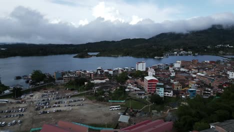 Luftdrohne-Erstklassig-Fliegen-über-Der-Stadt-Guatape-Antioquia-Kolumbianische-Hügel,-See,-Der-Das-Silberne-Wasser-Und-Geschmückte-Häuser-Darstellt