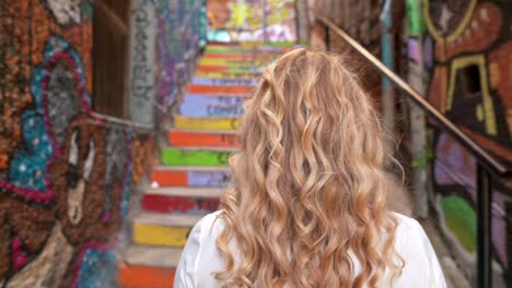 Close-up-of-a-young-blonde-girl-on-her-back-turning-to-camera-in-urban-painted-alleyway