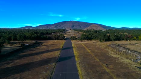 Aerial-view-low-over-Aztec-Ruins,-towards-the-Pyramid-of-the-sun-and-Temple-of-the-Moon,-sunny-evening-in-Teotihuacan,-Mexico