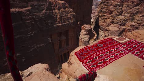 Traditional-carpets-on-cliff-in-foreground-of-Al-Khazneh-temple-in-Petra-ruins,-Jordan