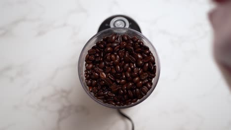 Person-Pouring-Coffee-Beans-On-Electric-Coffee-Grinder