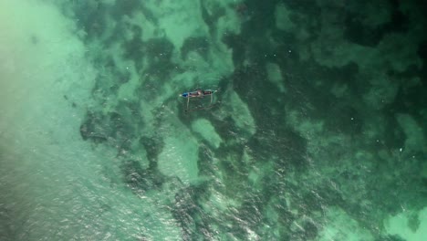 Aerial-top-down-of-a-fisherman-in-a-traditional-Indonesian-wooden-boat-fishing-in-clean-pristine-ocean-water