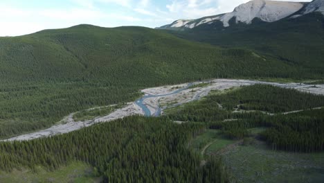 Revealing-shot-of-the-mountain-river-surrounded-by-mountains-and-forest-in-a-summertime