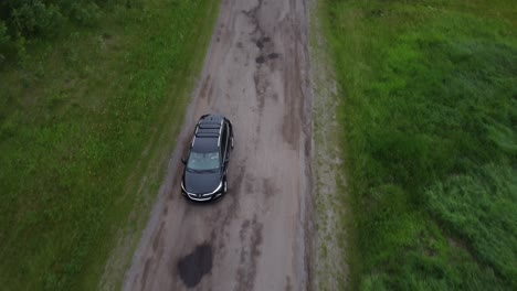 Vista-Frontal-Del-Enclave-De-Buick-Negro-Conduciendo-Por-La-Carretera-Forestal-Pasando-Por-Campos-De-Hierba