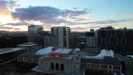 Union-Station-Denver,-sunset-drone-shot-with-classic-Travel-by-Train-neon-sign