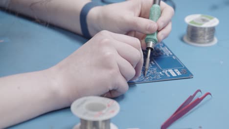 Side-shot-of-woman-placing-chip-in-blue-electronic-board-in-electronics-laboratory-with-small-clamp-while-wearing-a-security-antistatic-wrist-strap-for-safe-electronics-soldering