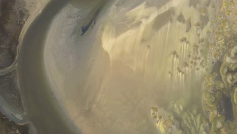 An-abstract-shot-of-curvy-water-bending-between-sand-and-mud-shore-of-Texel-island-in-Wadden-sea,-Netherlands