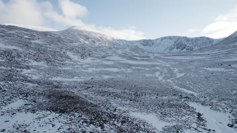 Aerial-drone-footage-reversing-and-rising-to-reveal-Cairngorm-Mountain-and-Coire-an-t-Sneachda-in-Cairngorms-National-Park,-Scotland-with-snow-covered-mountains-and-moorland-in-a-winter-landscape