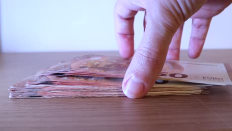 Closeup-of-male-hands-taking-a-lot-of-fifty-euro-notes-money-from-the-table