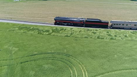 Eine-Parallele-Luftaufnahme-Eines-Antiken-Dampfpersonenzugs,-Der-An-Einem-Sonnigen-Tag-Durch-Ackerland-Fährt
