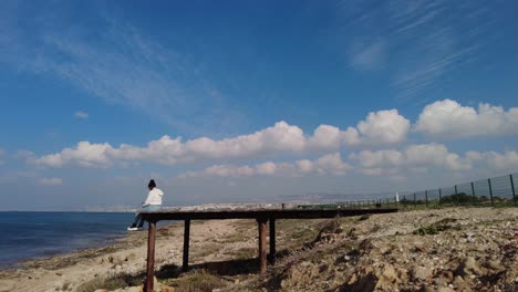 Ein-Mädchen-Sitzt-Am-Ende-Auf-Einem-Pier-Am-Strand-In-Griechenland