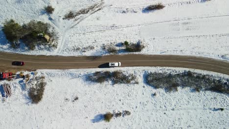 Aerial-view-of-a-van-driving-at-a-crossroad-in-rural-landscape-corered-with-snow-on-a-sunny-winter-day,-Dalmatian,-Croatia