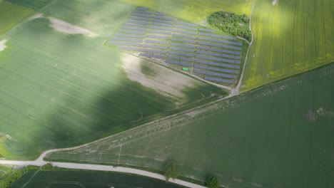 Aerial-high-altitude-establishing-shot-of-the-photovoltaic-solar-power-plant-in-the-middle-of-the-farm-fields