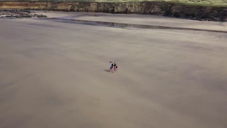Aerial-View-Of-Couple-Walking-On-The-Tranquil-Shore-Of-Godrevy-Beach-In-Cornwall,-England---drone-shot