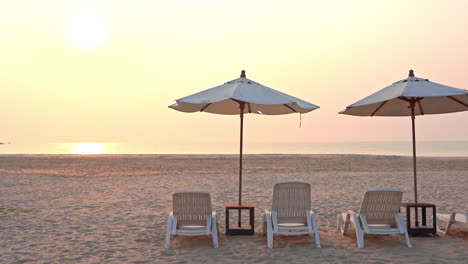 Leere-Liegestühle-Unter-Schattigen-Sonnenschirmen-Blicken-über-Den-Strand-Auf-Eine-Untergehende-Tropische-Sonne