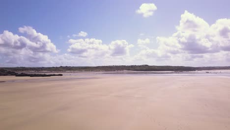 Couple-Walking-On-The-Sandy-Shore-Of-Godrevy-Beach-In-Cornwall,-England---drone-shot