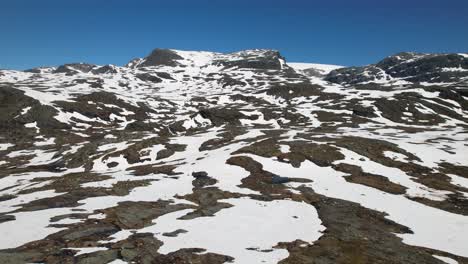 Schwenkdrohnenaufnahme-Eines-Schneebedeckten-Berges-Unter-Strahlend-Blauem-Himmel-In-Norwegen
