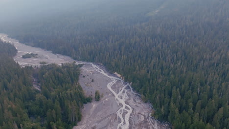 Aerial-footage-rotating-around-a-drying-riverbed-in-between-two-forests-in-the-morning-haze-in-Washington