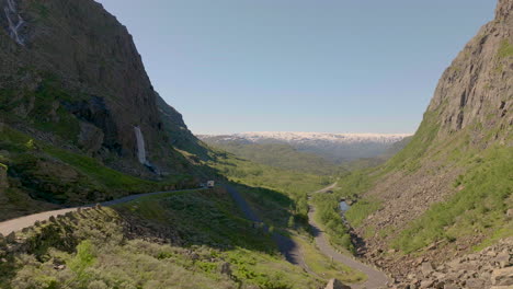 Drone-flying-low-over-old-mountain-road-verdant-valley-surrounded-by-Rugged-mountains,-Norway