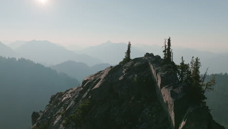 Aerial-footage-rotating-around-the-top-of-peak-of-a-mountain-that-is-covered-with-trees-and-boulders