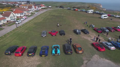 Aerial-drone-panning-shot-over-rows-of-supercars-parked-outside-Flamborough-Head-Lighthouse-in-Flamborough,-UK-at-daytime