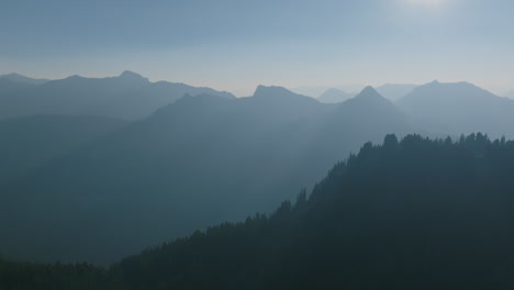 Aerial-footage-flying-towards-the-sunrise-in-the-Cascade-Mountains-with-the-ridges-and-trees-standing-out-against-the-haze