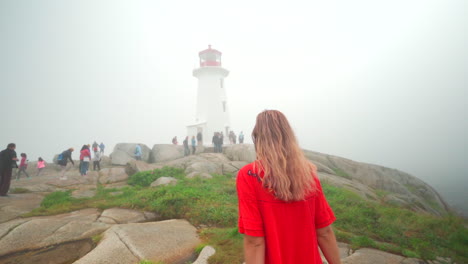 Young-woman-walking-towards-lighthouse-in-the-fog-on-an-overcast-day-in-Nova-Scotia,-Canada