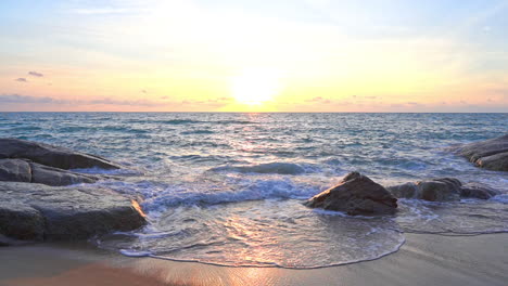 Ocean-waves-reflecting-the-colors-of-a-tropical-sunset-as-they-roll-into-shore-over-large-rocks