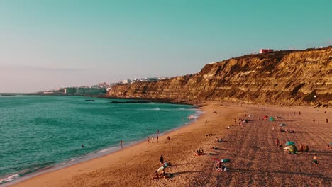 People-Doing-Activities-On-Wide-Foz-De-Lizandro-Beach-Under-High-Rocky-Ciffs,-Portugal