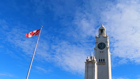 Clock-Tower-Building-Exterior-Facade-and-Canada-Flag-Waving-Swaying,-Montreal-Canada,-Low-Angle-View,-Blue-Sky-in-Background