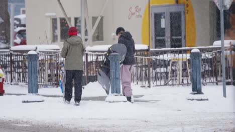 Zwei-Teenager,-Die-Ihre-Schlitten-Durch-Die-Verschneiten-Straßen-Einer-Kleinstadt-Tragen