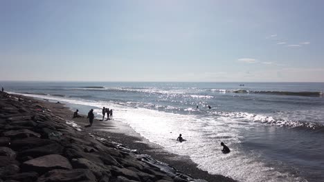 Kids-Bathing-in-the-Wild-Sea,-Bali-Indonesia-Water-Reflection,-Sun-and-Clear-Day,-Waving-Ocean-in-Ketewel,-Gianyar,-60-Fps