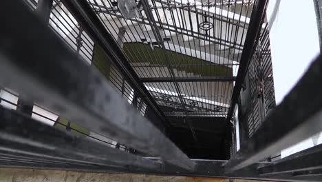 Vintage-elevator-in-typical-building-in-Old-Havana-ascending-and-stopping,-filmed-down-the-lift-shaft