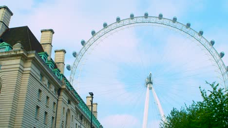 Panorámica-Suave-Cinematográfica-Del-Ojo-De-Londres-Contra-El-Cielo-Azul,-Las-Nubes-Y-El-Edificio-Del-Hotel-County-Hall,-Rodada-En-Rojo-Escarlata-w-5k