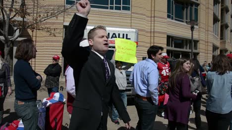 Un-Joven-Blanco-Con-Traje-Se-Burla-De-Los-Manifestantes-Anti-trump-Fuera-De-Un-Mitin-Político,-El-Caucus-Republicano-De-Iowa