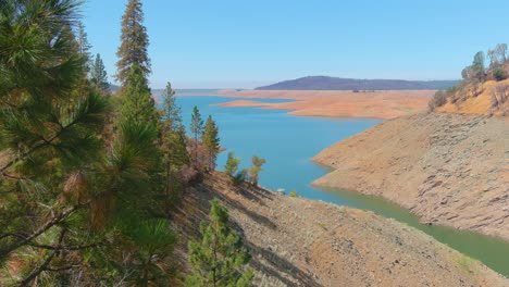 Erstaunliche-Luftaufnahme-über-Dem-Von-Dürre-Betroffenen-Kalifornischen-See-Oroville-Mit-Niedrigem-Wasserstand,-Zurückweichender-Küstenlinie-Und-Verbrannten-Bäumen-Und-Wäldern