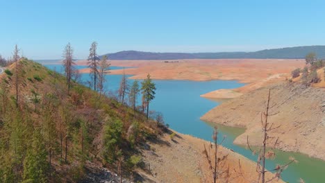 Inquietante-Antena-Sobre-El-Lago-Oroville-De-California-Azotado-Por-La-Sequía-Con-Bajos-Niveles-De-Agua,-Costa-En-Retroceso-Y-árboles-Y-Bosques-Quemados