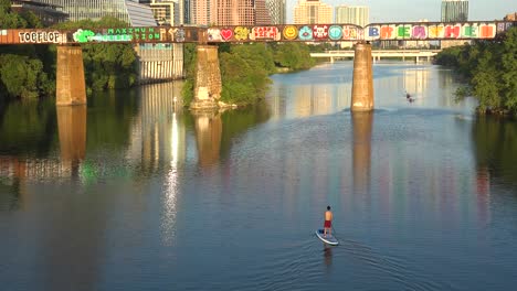 Un-Paddleboarder-Rema-Por-El-Río-Colorado-Mientras-Se-Revela-El-Horizonte-Del-Centro-De-Austin,-Texas