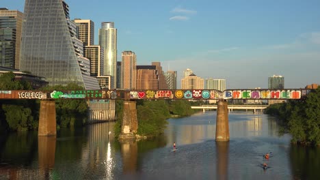 Un-Paddleboarder-Rema-Por-El-Río-Colorado-Frente-Al-Horizonte-Del-Centro-De-Austin,-Texas