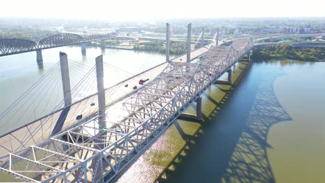 Antena-Sobre-Los-Puentes-Del-Río-Ohio-Con-El-Horizonte-Del-Centro-De-Louisville,-Kentucky-Distante-Sugiere-Infraestructura